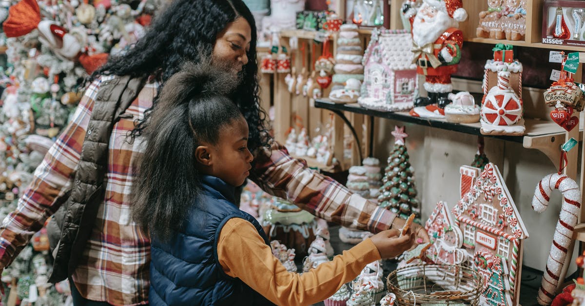 Prepare and backup Wii U for sale - Young smiling ethnic woman with girl choosing gifts near Christmas tree in souvenir shop