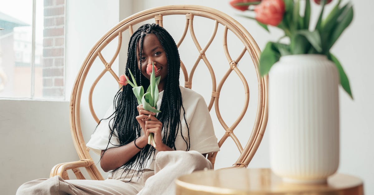 Presents effects during free time - Smiling young black lady smelling bunch of tulips while sitting on chair
