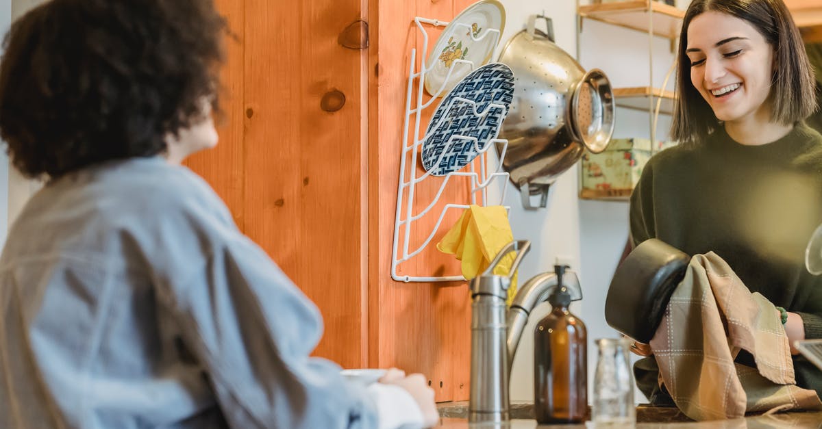 Pressure Plates and Chat [duplicate] - Cheerful young women speaking with each other and smiling in kitchen with different utensil