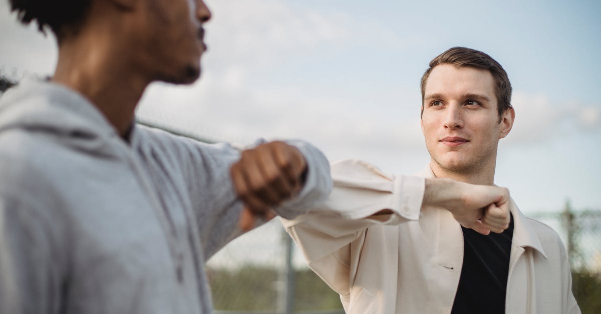 Preventing the spread of infection - Serious multiethnic male friends doing elbow bump for protection and avoiding spreading of coronavirus infection and looking at each other