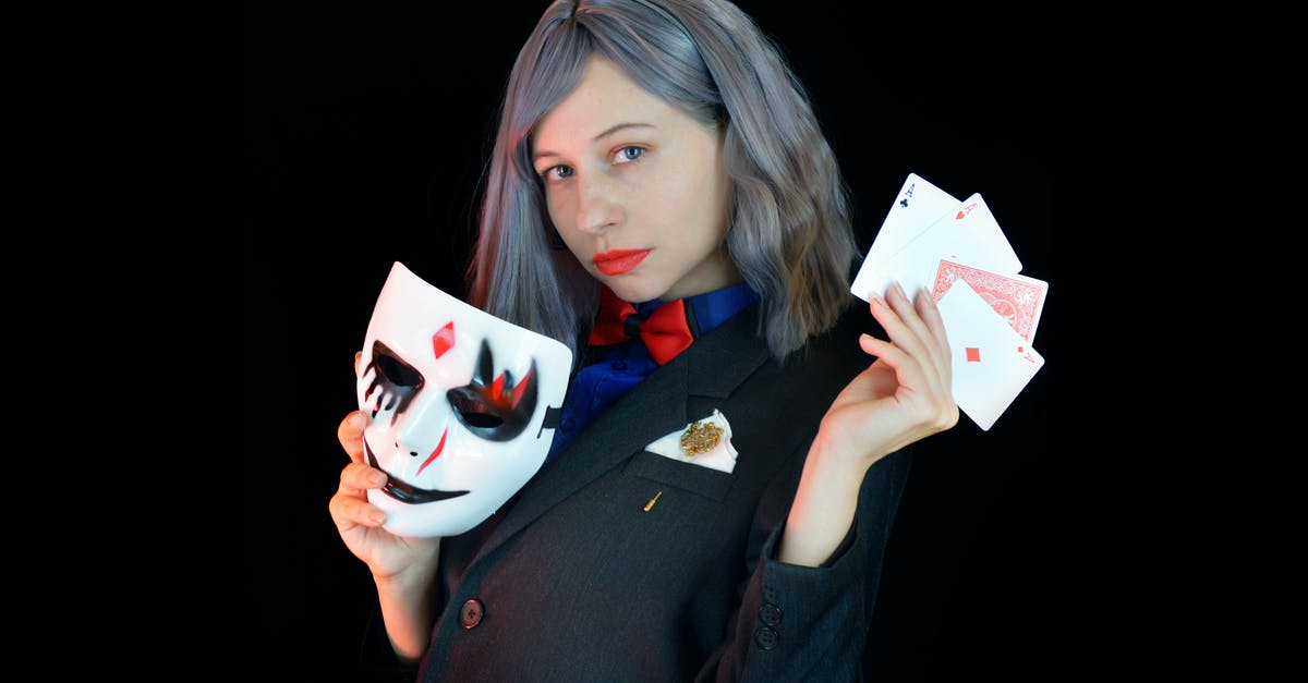 Purifier and 'appearing as witchcraft user': what happens? - Side view of serious young female casino dealer in classy suit with bow tie holding face mask and cards in hands and looking at camera against black background