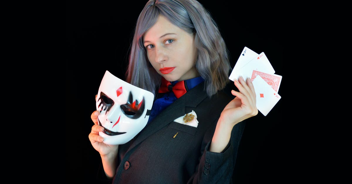 Purifier and 'appearing as witchcraft user': what happens? - Side view of serious young female casino dealer in classy suit with bow tie holding face mask and cards in hands and looking at camera against black background Purifier and 'appearing as witchcraft user': what happens? - Side view of serious young female casino dealer in classy suit with bow tie holding face mask and cards in hands and looking at camera against black background