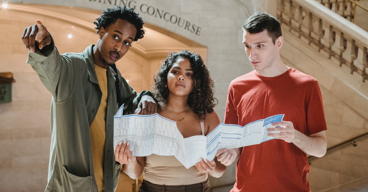 "Off the Record" mission not showing in terminal - Young African American male tourist pointing away while searching for direction with diverse fiends standing in railway station terminal with paper map in hands "Off the Record" mission not showing in terminal - Young African American male tourist pointing away while searching for direction with diverse fiends standing in railway station terminal with paper map in hands