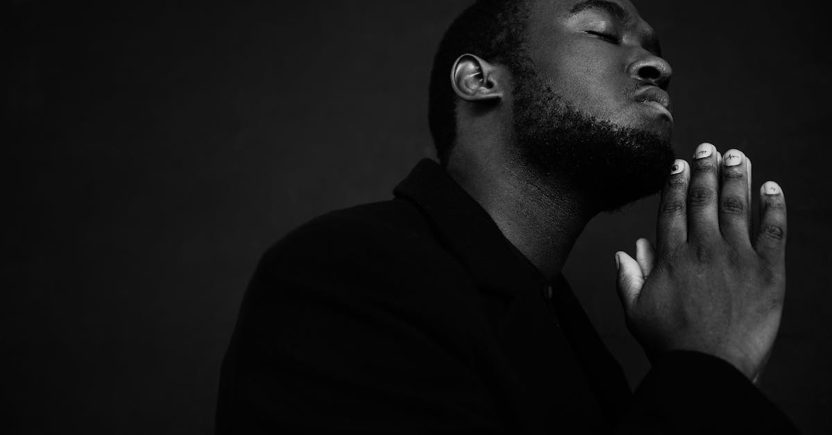 Realm of the mad god closed realm question - Monochrome handsome unshaven African American male in black suit praying with hands clasped under chin Realm of the mad god closed realm question - Monochrome handsome unshaven African American male in black suit praying with hands clasped under chin