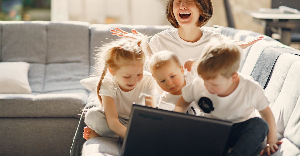 Realm of the Mad god is too laggy to play - Stressed woman asking for help while sitting with small children playing on laptop together on sofa in living room