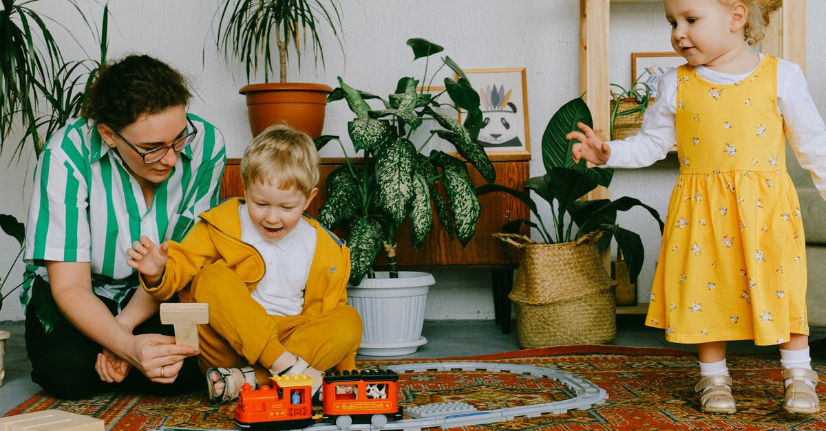 Rec room people automatic repawn in own flag game - Mom and adorable little brother and sister in casual wear gathering in cozy living room during weekend and having fun together while playing with plastic railway Rec room people automatic repawn in own flag game - Mom and adorable little brother and sister in casual wear gathering in cozy living room during weekend and having fun together while playing with plastic railway