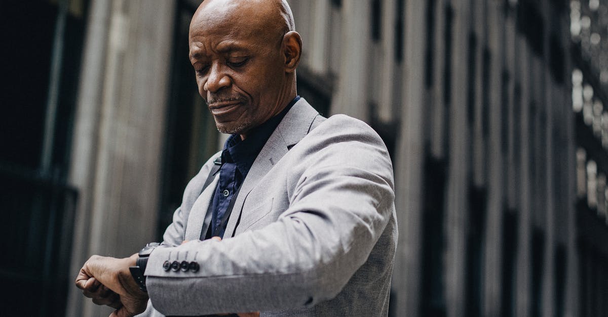 Redstone repeater delay if activated - Serious African American businessman in formal suit looking at wristwatch while standing outside modern business center building