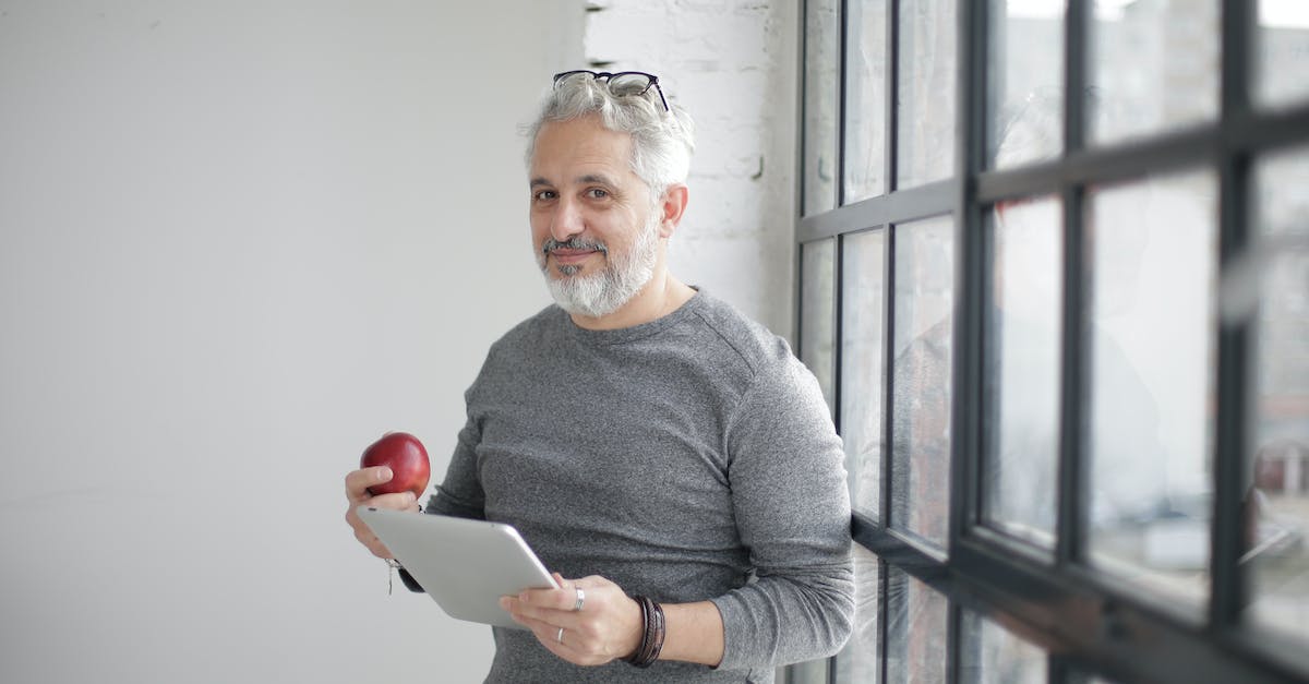 Reduced Mana reserved - how does it work? - Smiling middle aged man using tablet and holding apple near window in office