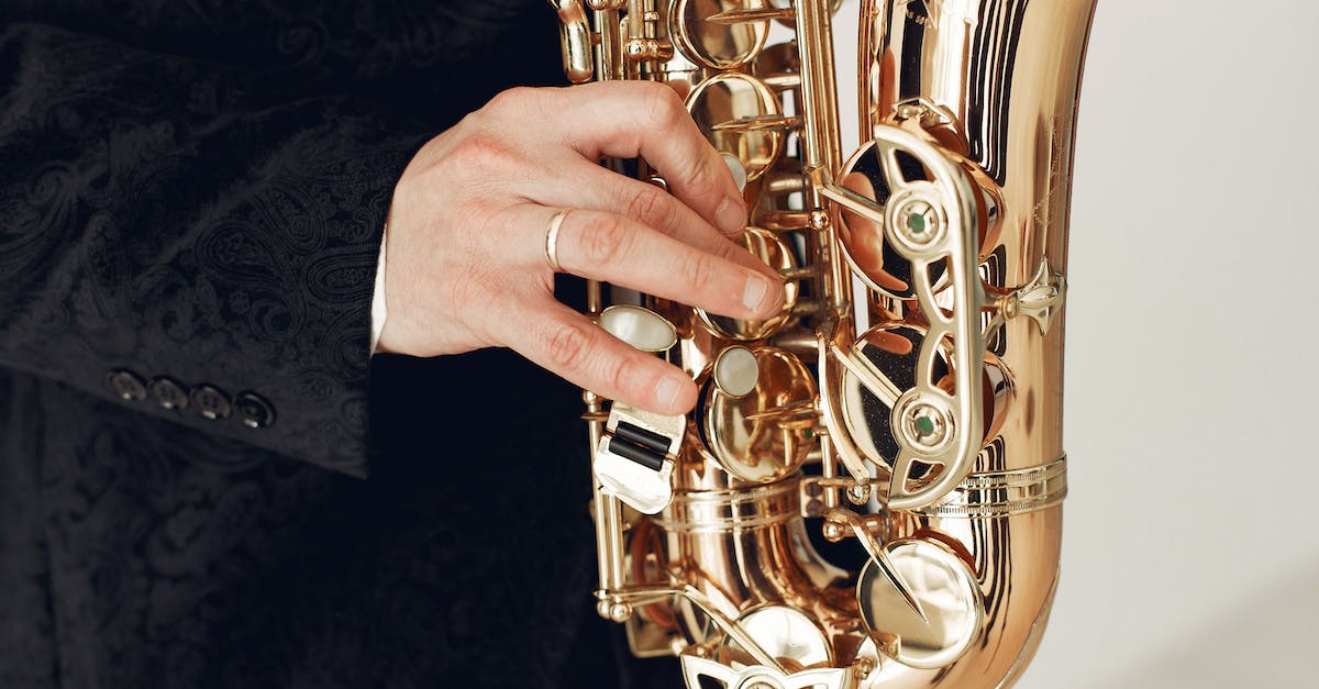 Reincarnating with gold talents - Unrecognizable talented male artist wearing concert costume playing jazz melody on saxophone standing against white background during rehearsal or music show