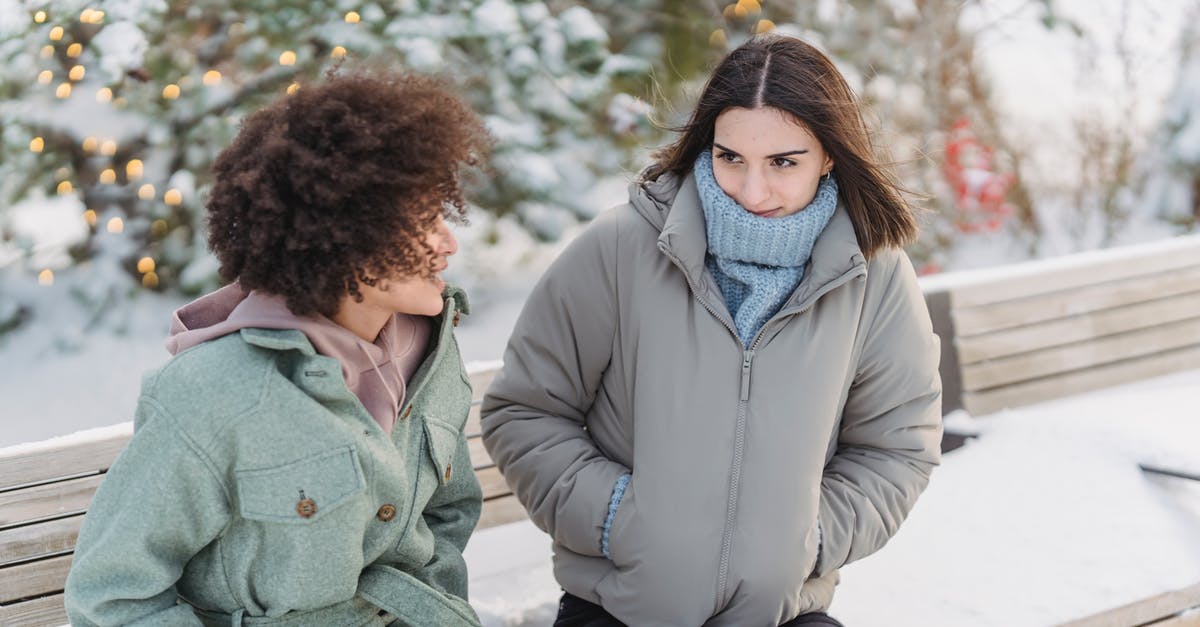 Removing freeze time forever - Diverse female friend talking on bench in winter park Removing freeze time forever - Diverse female friend talking on bench in winter park