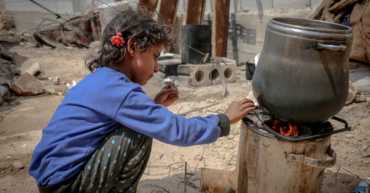 Removing Lightnings's extra damage by fire? - Side view of ethnic kid sitting near furnace with metal pan placed on fire in daylight in poor destroyed district Removing Lightnings's extra damage by fire? - Side view of ethnic kid sitting near furnace with metal pan placed on fire in daylight in poor destroyed district