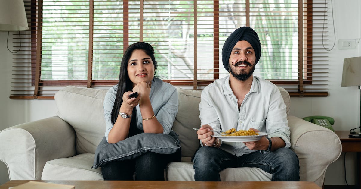 Replays - Switch YouTube account that movies are uploaded to? - Positive male with plate of food and female in casual clothes sitting on sofa in living room and watching TV at home