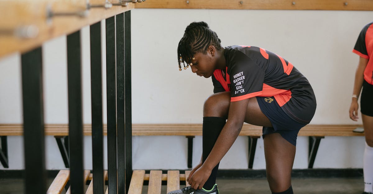 Richest clubs on football manager 2014 - Side view of teenager wearing team sportswear and sneakers standing on benches and preparing for training in gym while looking away pensively