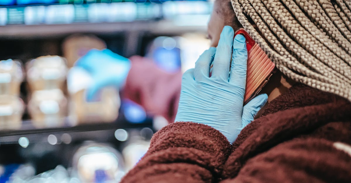 Select phenotypes to use for empires - Side view of crop African American female customer in latex gloves with braids having phone call while picking food from shelf in grocery store