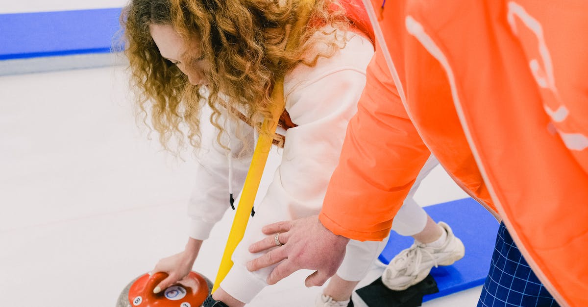 Select player not in a specific position - Man instructor fixing position of hand of female curling player Select player not in a specific position - Man instructor fixing position of hand of female curling player