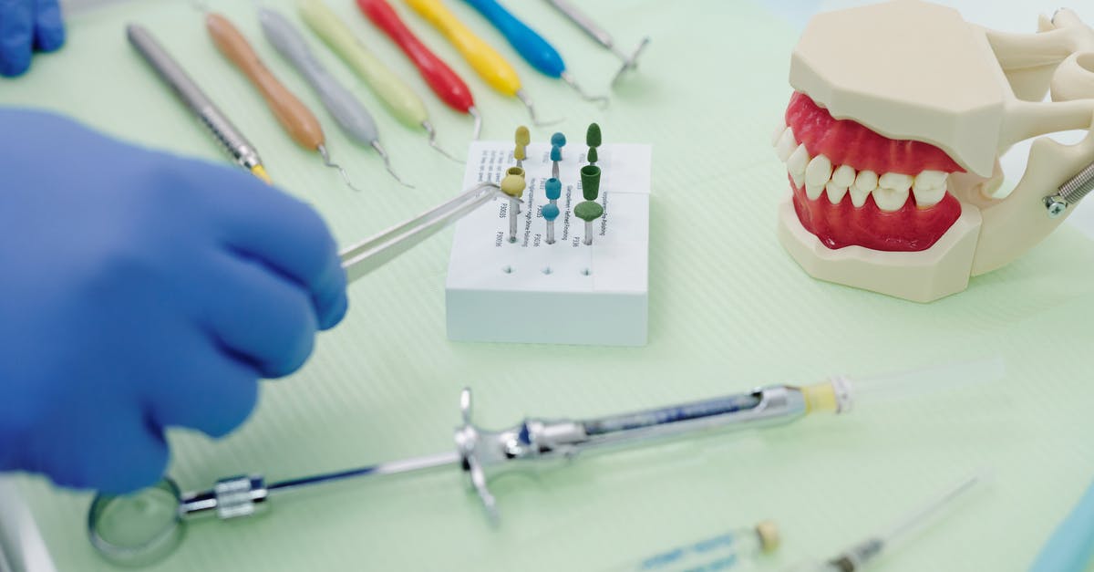 Set settlement spawn point - From above of crop faceless orthodontist in latex gloves and tweezers working at medical table with cast jaw and set of syringes near periodontal scalers