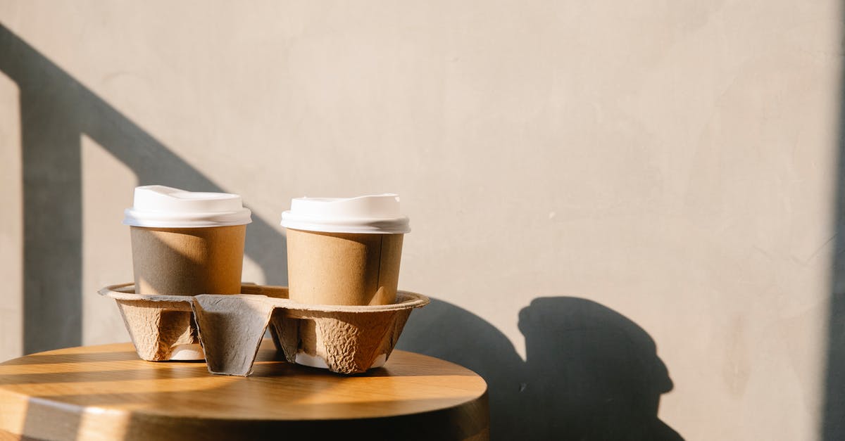 Set Xbox controllers order on Windows - Cofee paper cups with plastic lids on holder tray on brown wooden table casting a shadow at sunny day