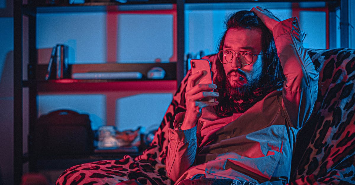 Should I be concerned about a possible counterfeit DS game? - Surprised adult unshaven ethnic male in eyeglasses with pouting lips browsing internet on cellphone while touching head and sitting on comfortable armchair near shelf in apartment with neon light