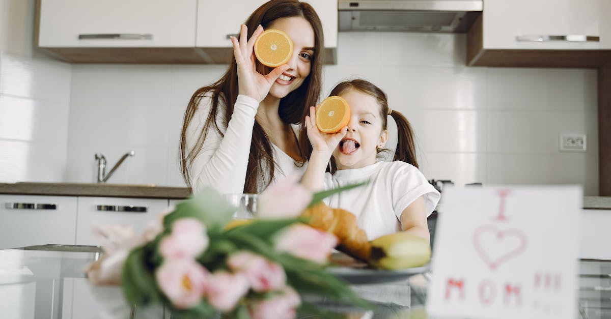 Should I eat corpses or destroy them? - From below of cheerful mother and daughter in domestic clothes smiling and playing with oranges while sitting together at table with bouquet of tulip and drawing of child