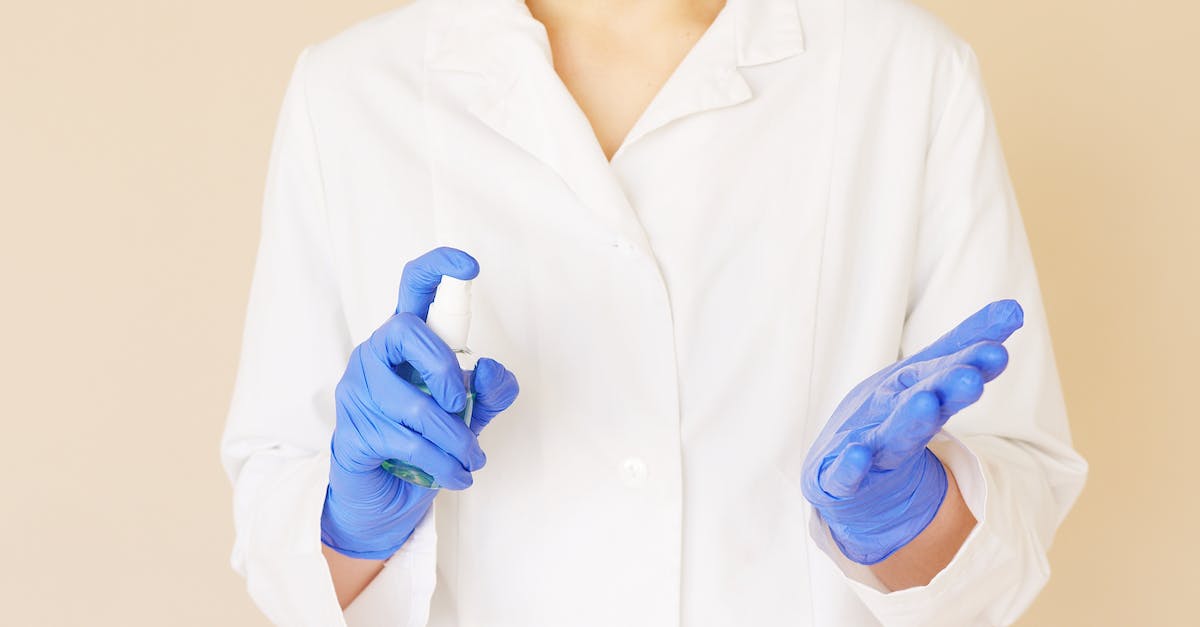 Should I spray or fertilize my crops? - Crop unrecognizable hospital worker in white uniform spraying antiseptic liquid over hands in blue latex gloves