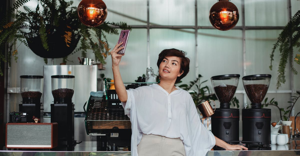 Should I use duplicate units to raise SA or unlock potential routes? - Cheerful Asian female with short brown hair in casual clothes standing against coffee machine and taking selfie on smartphone