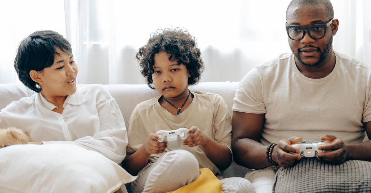 Should I watch the TV series before playing Game of Thrones? - Focused ethnic child and dad in sleepwear using gamepads for playing video games on console via TV while sitting on comfortable couch together with mom Should I watch the TV series before playing Game of Thrones? - Focused ethnic child and dad in sleepwear using gamepads for playing video games on console via TV while sitting on comfortable couch together with mom
