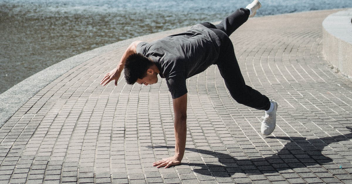 Show sources for tile values - Anonymous young ethnic male athlete balancing on hand with raised leg near city river in summer