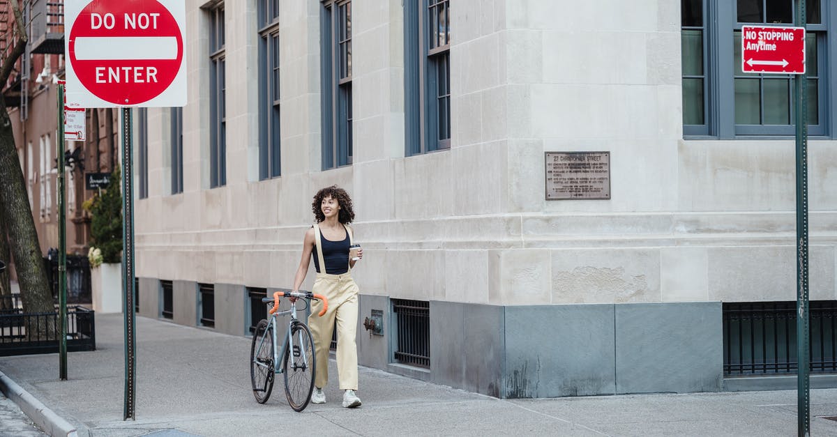 Show the direction of one-way roads - Contemplative ethnic woman with coffee and bike walking on pavement