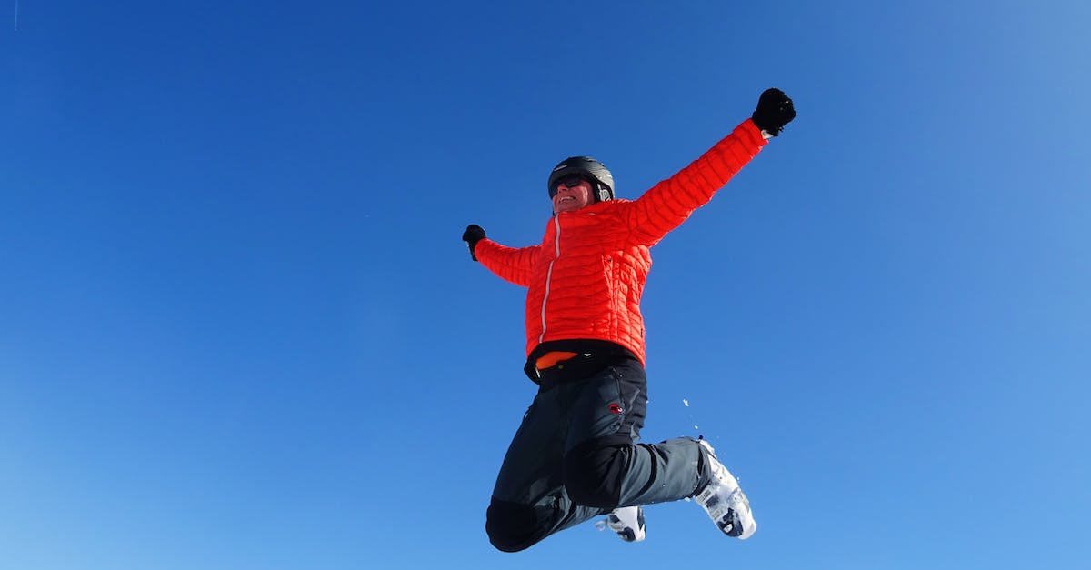 Ski Jumping Pairs? - Man in Orange Zip Jacket and Black Pants Jumping Under Blue Sunny Sky