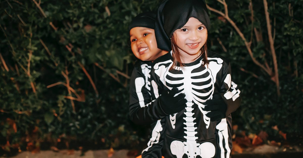 Some females don't have the right skeleton - Happy best multiethnic female friends in Halloween costumes embracing against plants in town at dusk