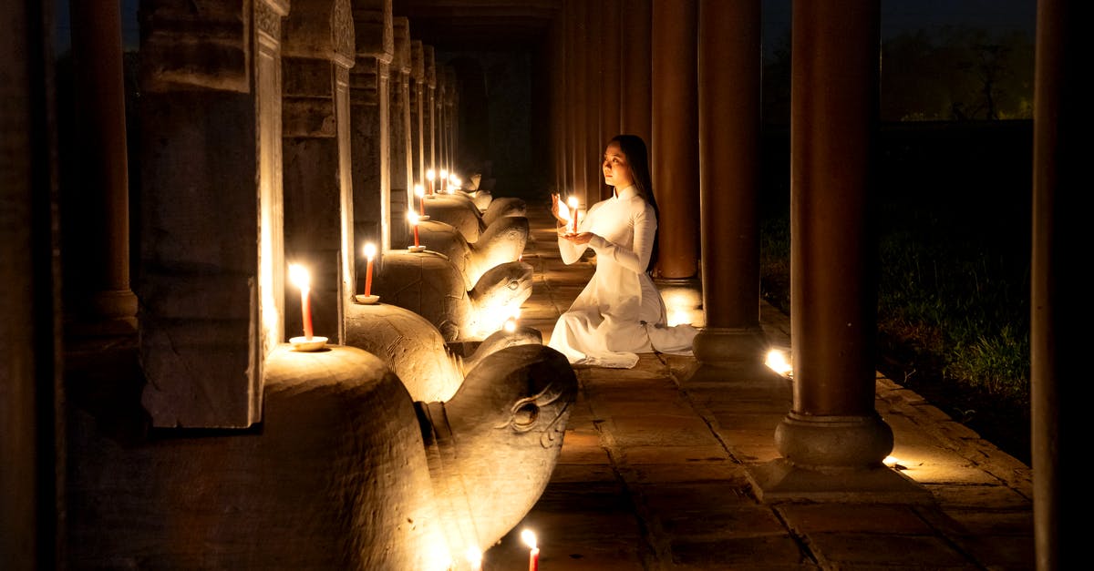 Soul Vessel in Dark Souls 2 - Side view of tranquil Asian female with burning candle in hands praying near stone turtles with steles in dark time