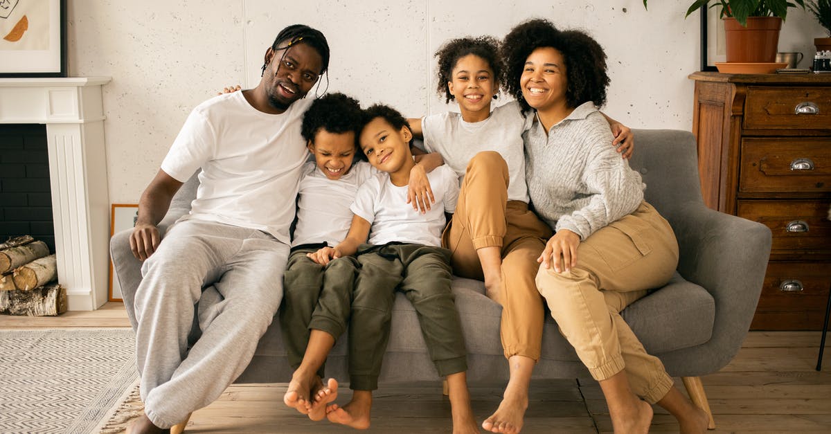 Sparing Sans before he asks to be spared? - Full body of cheerful African American parents with children looking at camera while sitting on sofa in room with fireplace