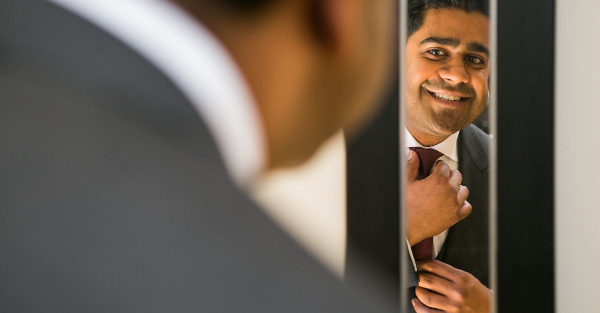 Special 8-Crown Not Appearing - Crop ethnic male in elegant suit preparing for special festive event while adjusting tie and looking at mirror Special 8-Crown Not Appearing - Crop ethnic male in elegant suit preparing for special festive event while adjusting tie and looking at mirror