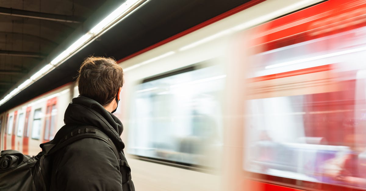 Stations with orbit making move too fast - Side view of faceless male passenger in protective mask wearing warm outerwear standing on platform of metro station near train Stations with orbit making move too fast - Side view of faceless male passenger in protective mask wearing warm outerwear standing on platform of metro station near train