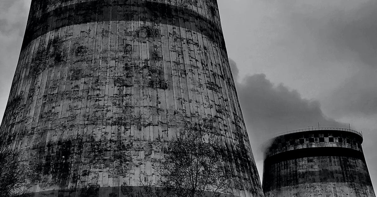 Steam stays in system language - Old draft wet cooling towers in city industrial district on cloudy sky