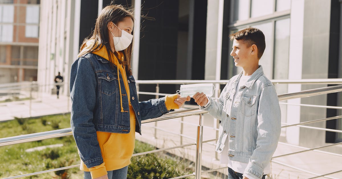 Stop sharing my COC-account - Side view of happy young boy in casual clothes smiling and standing against elder sister in medical mask on city street while taking face mask