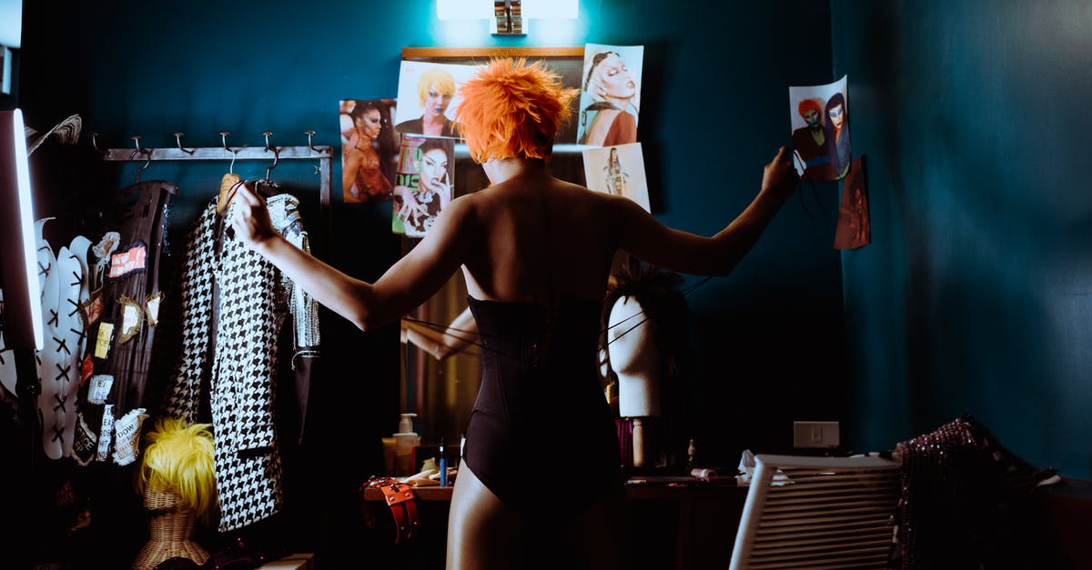 Strange lag in Mirror's edge - Back view of anonymous androgynous dancer in stage clothes and wig tying corset while standing near mirror in dark dressing room