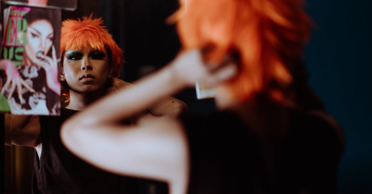 Strange lag in Mirror's edge - Back view crop provocative female with bright makeup in black dress putting on orange wig and looking in mirror Strange lag in Mirror's edge - Back view crop provocative female with bright makeup in black dress putting on orange wig and looking in mirror