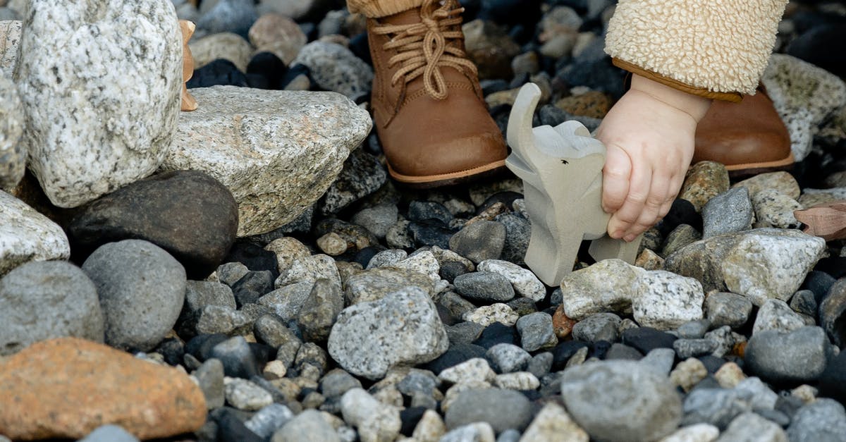 Succeed in baby rocking game in Tomodachi? - Unrecognizable little child in warm clothes and brown boots playing with stone toy of elephant between stones on seashore in winter Succeed in baby rocking game in Tomodachi? - Unrecognizable little child in warm clothes and brown boots playing with stone toy of elephant between stones on seashore in winter