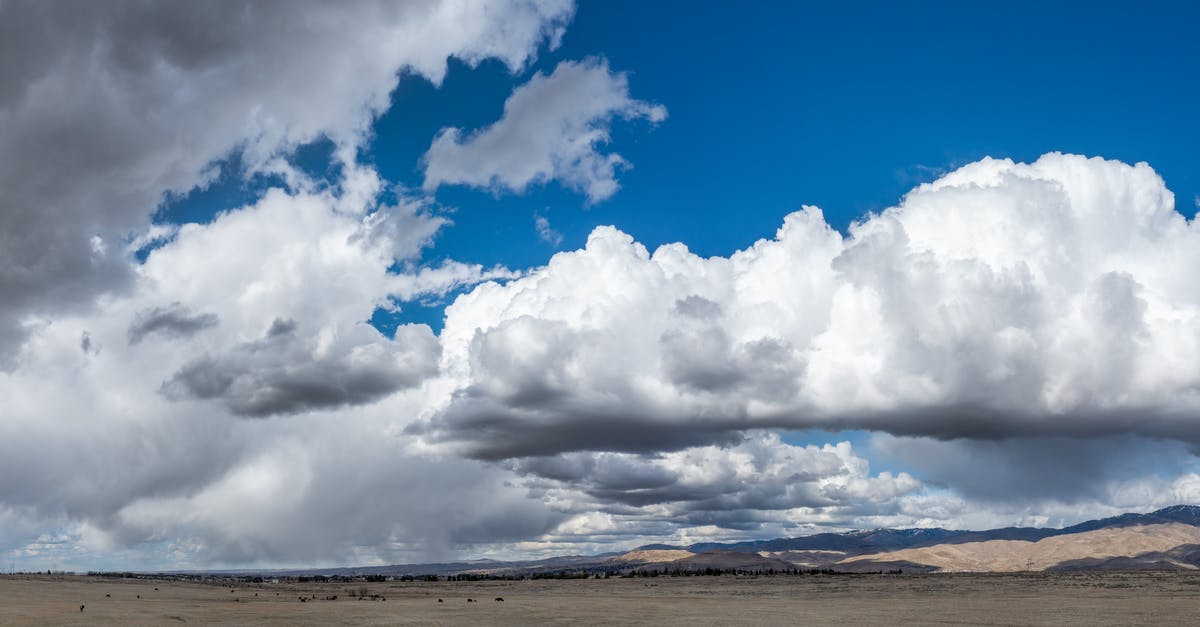 Summoning falling grass in an area - Panoramic view of white cumulus clouds floating on blue sky over vast grassy field against hilly area in sunny nature Summoning falling grass in an area - Panoramic view of white cumulus clouds floating on blue sky over vast grassy field against hilly area in sunny nature