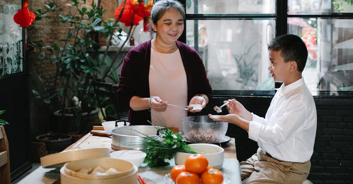 Super Meat Boy warp zone not completed? - Side view of positive Asian preteen boy sitting at table in kitchen and helping smiling mature grandmother to prepare traditional Chinese dumplings for dinner