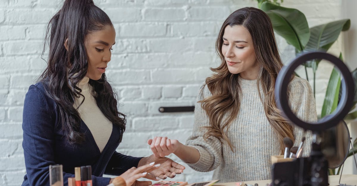Test for range of values in a datatag using testforblock - Young positive multiethnic female bloggers testing makeup products while sitting at table and recording vlog on smartphone placed on tripod with ring light