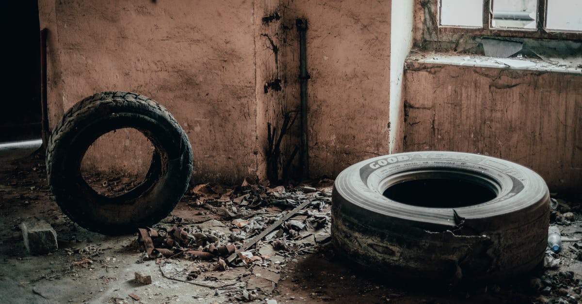 Tires stuck in the floors, what is the use? - Weathered tires on dirty floor near shabby wall with peeling plaster and old window in abandoned building with rubbish and ruins Tires stuck in the floors, what is the use? - Weathered tires on dirty floor near shabby wall with peeling plaster and old window in abandoned building with rubbish and ruins