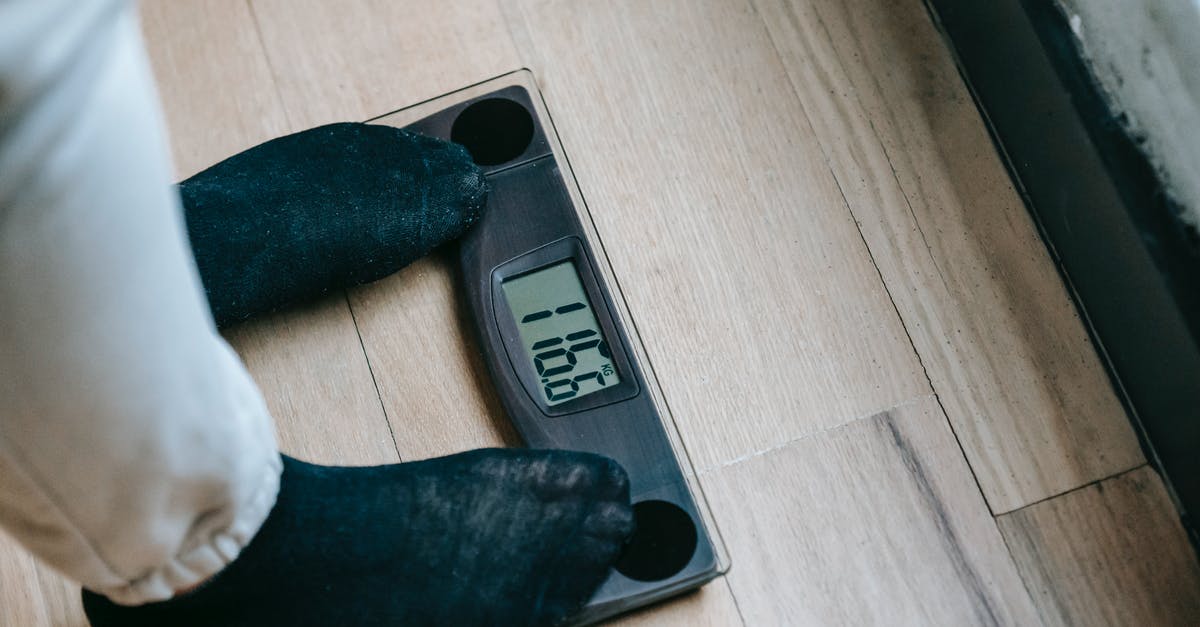 Training Mode: NPC on control option - From above of unrecognizable person in socks standing on electronic weighing scales while checking weight on parquet during weight loss