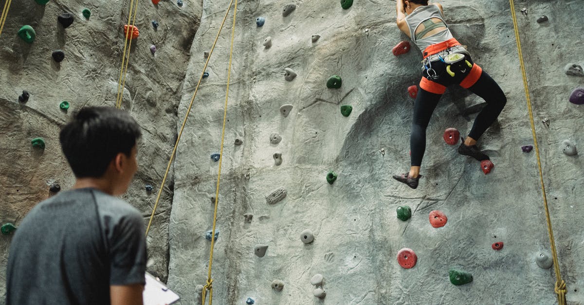 Training Mode: NPC on control option - Young coach controlling climber training on rocky wall Training Mode: NPC on control option - Young coach controlling climber training on rocky wall