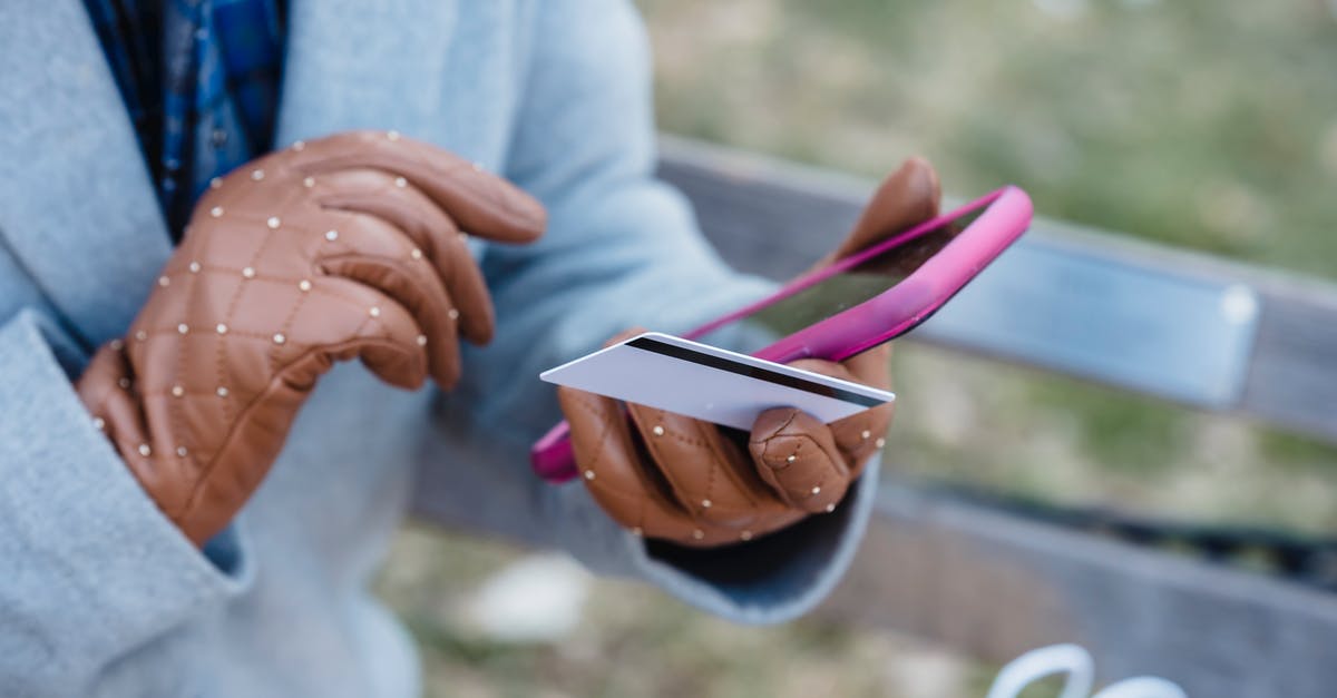 Transfer/Claim In-App Purchase to/on Another Device - Crop anonymous female in blue coat and leather gloves with credit card making online purchase via smartphone while sitting on bench in city park Transfer/Claim In-App Purchase to/on Another Device - Crop anonymous female in blue coat and leather gloves with credit card making online purchase via smartphone while sitting on bench in city park