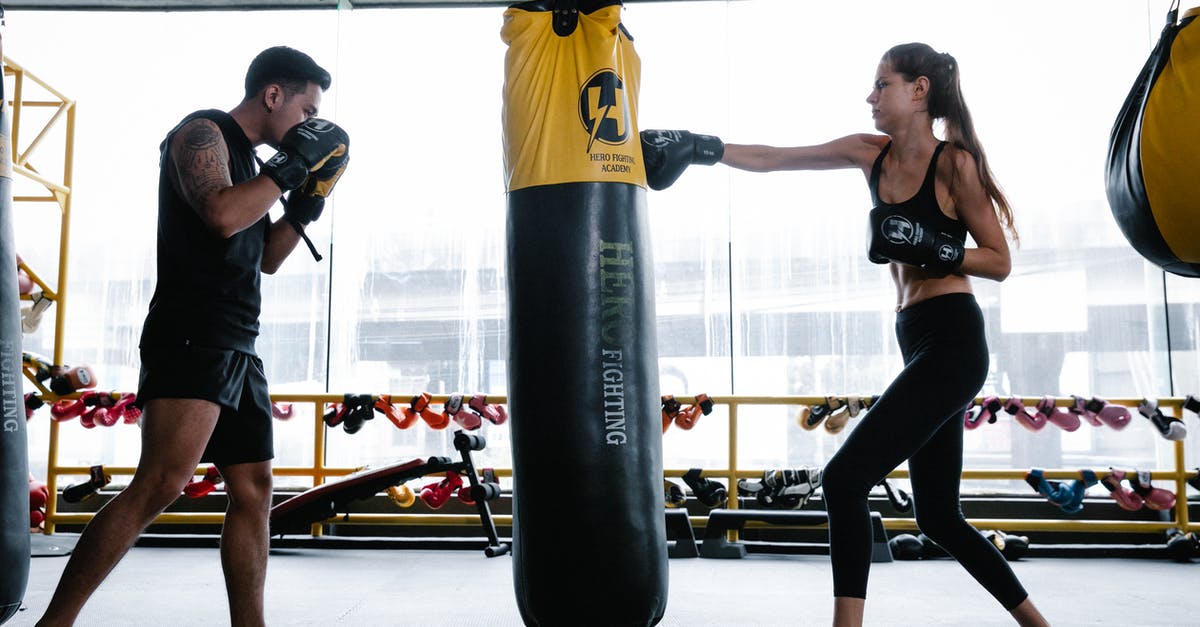 Two-Hand vs Power Stance in DkS2? - Side view of strong young female and male boxers in sportswear and protective gloves practicing punches on hanging heavy bag while training together in gym