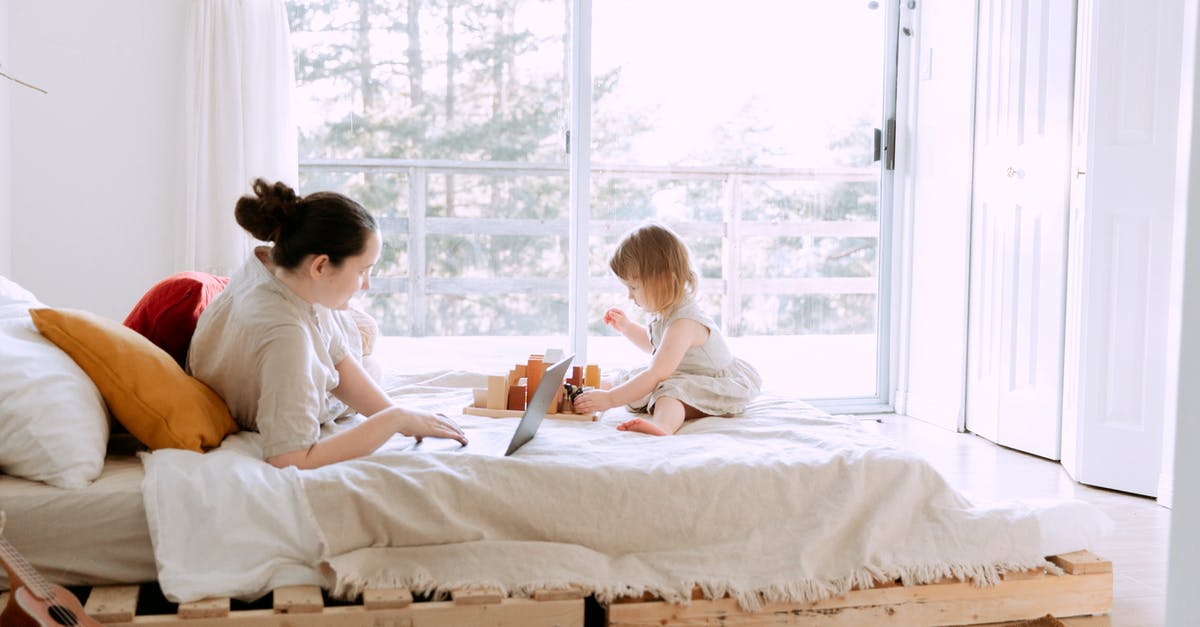 Typing into signs crash the game - Side view of young focused female in casual clothes lying in bed and using laptop while daughter playing sitting nearby on sunny morning Typing into signs crash the game - Side view of young focused female in casual clothes lying in bed and using laptop while daughter playing sitting nearby on sunny morning
