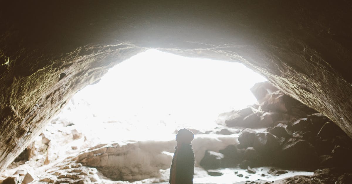 Unable to activate Fabled Cave - Side view of unrecognizable traveler standing in mountain cave in light of bright sun and admiring stone formation