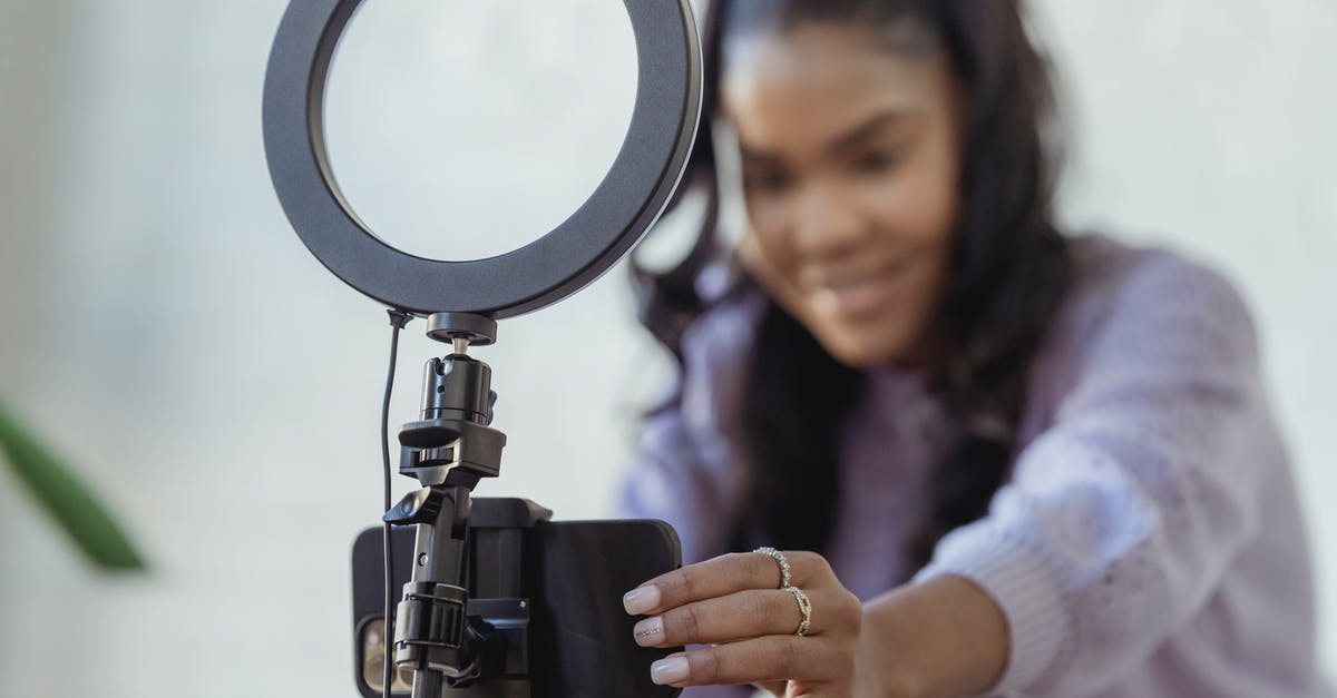 Unable to join online games of Among Us due to Parental Controls that were never set up? - Cheerful young African American female blogger in stylish sweater smiling while setting up camera of smartphone attached to tripod with ring light before recording vlog